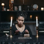 A young woman sits at a table with candles, conducting a mystical seance with tarot cards.